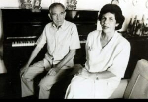 Maestro José Raab e Sarah Pereira Barbosa sentado em frente a um piano em sala de estar, em fotografia antiga em preto e branco.