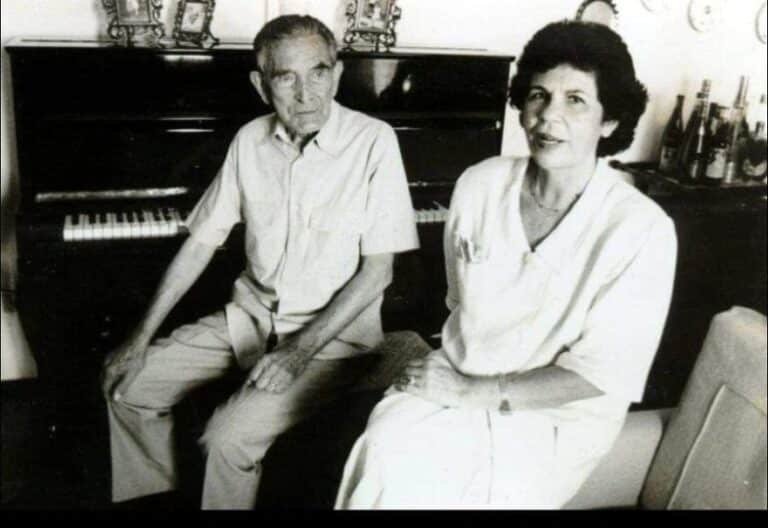 Maestro José Raab e Sarah Pereira Barbosa sentado em frente a um piano em sala de estar, em fotografia antiga em preto e branco.