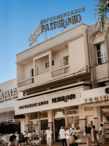 Fachada do Supermercados Pastorinho em Araçatuba-SP, com letreiro no topo do prédio e movimento de pessoas na calçada em frente ao supermercado.
