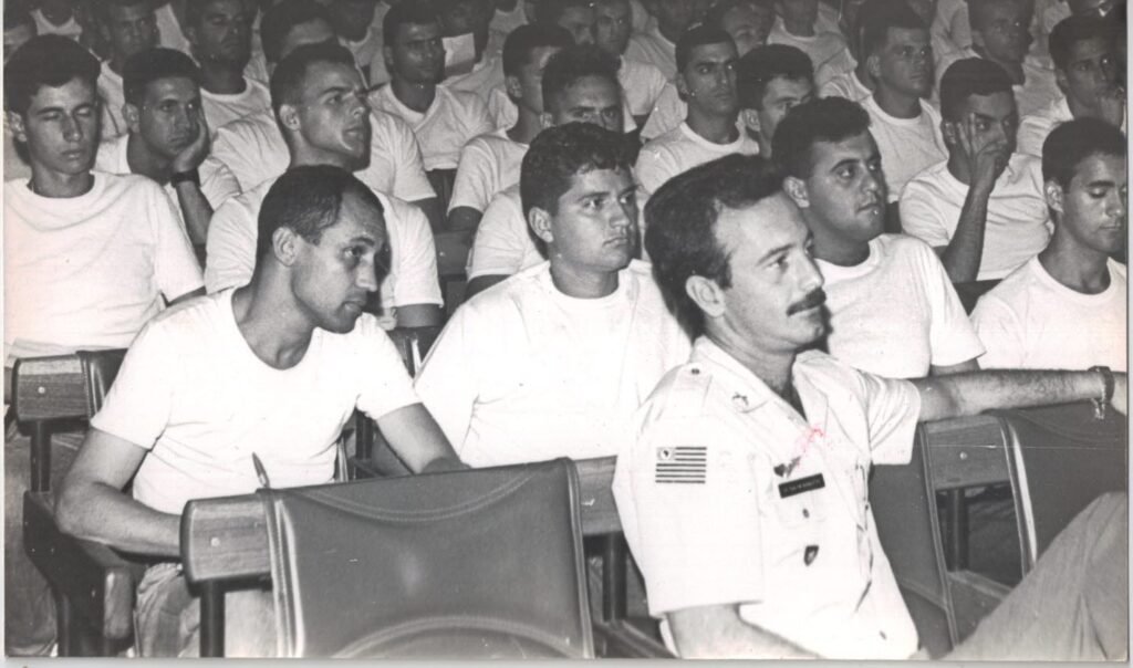 Na imagem histórica, o então comandante da Polícia Militar de São Paulo, Nicoletti Pascoal, aparece em destaque durante uma palestra ou instrução. Ele está em primeiro plano, vestindo farda de oficial, com a insígnia do estado de São Paulo visível no ombro.